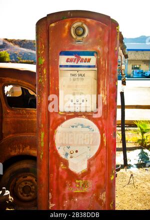 Pompa a gas a chevron rossa disutilizzata con vettura arrugginita parzialmente in vista Foto Stock