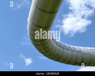 raccordo a gomito per tubi sopraelevati in vista ad angolo basso con segmenti di espansione. tubi di riscaldamento per distretto rivestiti in alluminio. cielo blu. luce solare per molle luminose Foto Stock