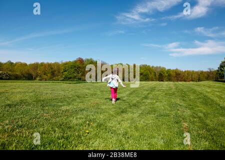 Una ragazza felice in abiti luminosi corre attraverso un campo in primavera Foto Stock