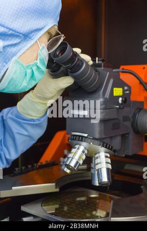 L'ispettore che effettua il controllo in entrata le fette di silicio con chip al microscopio in camera libera. Foto Stock