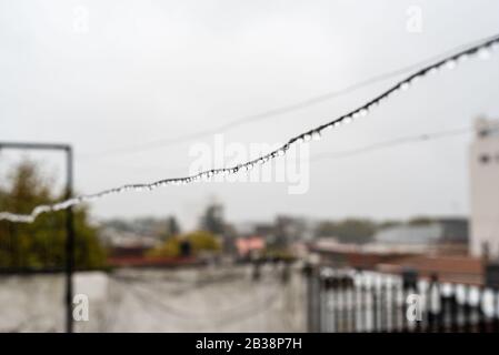 Filo di clothesline pieno di piccole gocce in una giornata piovosa con una messa a fuoco selettiva nel centro profondità di campo molto poco profonda Foto Stock