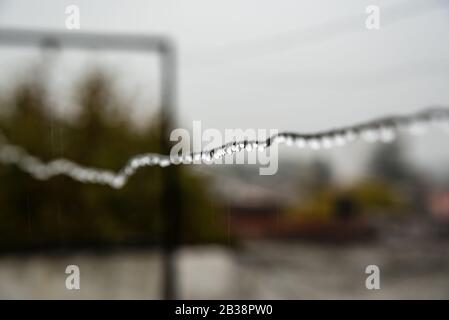 Filo di clothesline pieno di piccole gocce in una giornata piovosa con una messa a fuoco selettiva nel centro profondità di campo molto poco profonda Foto Stock