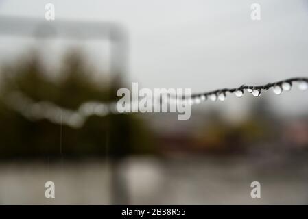 Filo di clothesline pieno di piccole gocce in una giornata piovosa con una messa a fuoco selettiva nel centro profondità di campo molto poco profonda Foto Stock