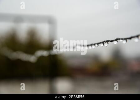 Filo di clothesline pieno di piccole gocce in una giornata piovosa con una messa a fuoco selettiva nel centro profondità di campo molto poco profonda Foto Stock