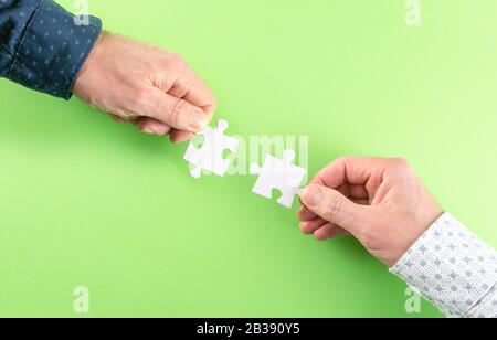 mani di due uomini d'affari che collegano pezzi di puzzle corrispondenti contro sfondo verde, partnership di affari e concetto di lavoro di squadra Foto Stock