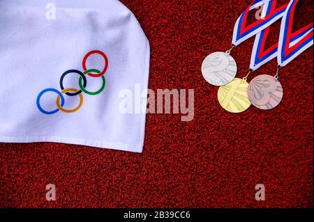 TOKYO, GIAPPONE, 5 MARZO. 2020: Set di medaglie e anelli olimpici, pista di atletica rossa in background Foto Stock