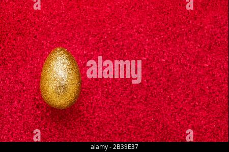 Uovo d'oro di Pasqua su sfondo rosso blured. Concetto di festa di Pasqua. Vista dall'alto, copia spazio per il testo. Foto Stock