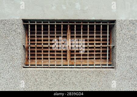 Vecchia griglia di ventilazione in legno arrugginita con barre di ferro di protezione su vecchio muro di cemento magazzino, Hualien, Taiwan. Minimalista, semplicità Foto Stock