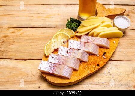 Ingredienti di pesce e patatine su tavola e tavola di legno. Cucina tradizionale britannica, un bicchiere di birra. Foto Stock