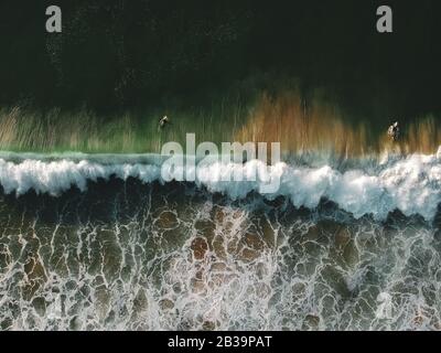 Vista sul drone delle splendide onde turchose del mare che si infrangono sulla costa sabbiosa. Foto aerea della spiaggia dorata che incontra acque blu profonde dell'oceano e onde schiumose Foto Stock