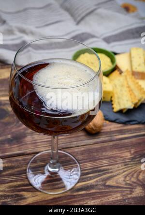 Bicchiere di birra rossa dell'abbazia belga e piatto di marmo con formaggi prodotti da monaci di latte vaccino con fenugreek e semi di senape da vicino Foto Stock