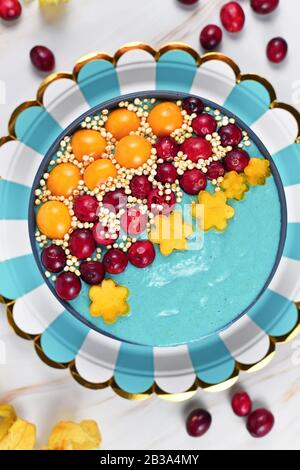 Ciotola di frullato di frutta blu tinto con polvere di spirulina naturale decorata con mirtilli rossi, phisalis e frutti kaki e grani di quinoa purè Foto Stock