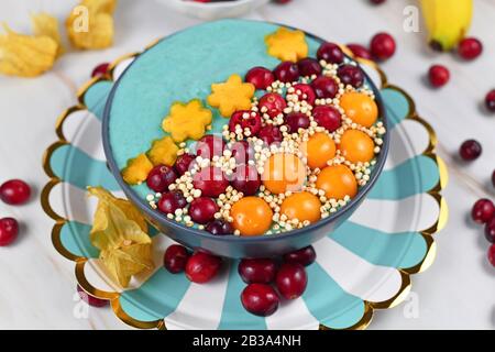 Ciotola di frullato di frutta blu tinto con polvere di spirulina naturale decorata con mirtilli rossi, phisalis e frutti kaki e grani di quinoa purè Foto Stock