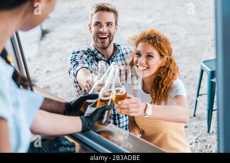 focus selettivo di chef multiculturali che tostano bottiglie di birra vicino a clienti soddisfatti Foto Stock