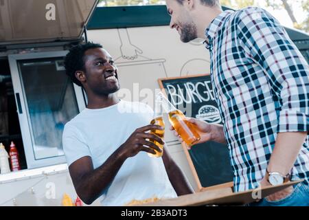 vista a basso angolo di uomini multiculturali felici tostare bottiglie di birra Foto Stock