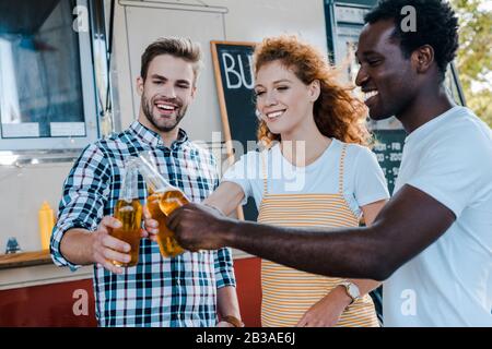 fuoco selettivo di uomini multiculturali felici che si inclinano con donna rossa vicino al camion del cibo Foto Stock