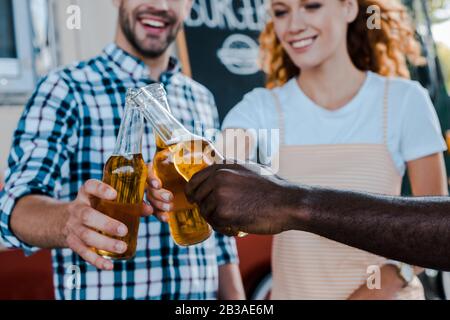 vista corta di uomini multiculturali felici che si abbinavano con donna rossa vicino al camion del cibo Foto Stock