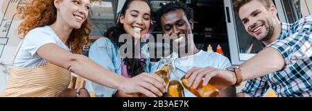 scatto panoramico di amici multiculturali felici bottiglie di clinking con birra vicino al camion del cibo Foto Stock