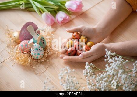 Sopra la vista di donna irriconoscibile che tiene una manciata di uova di quaglie al tavolo di legno mentre prepara le uova di Pasqua per le decorazioni Foto Stock