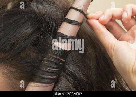 Il parrucchiere sta facendo capelli ricci. Uno styling dei capelli usando un waver del wand di curling della ceramica. Giovane donna sta styling i suoi capelli castani diritti Foto Stock