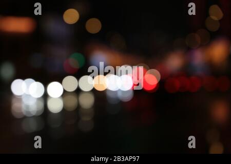 Luci sfocate dei fari della vettura sulla strada notturna della città durante la pioggia. Sfondo astratto colorato Foto Stock