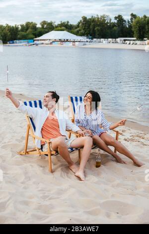 felice coppia interracial seduto in chaise lounges e tenuta sparklers mentre riposa sulla spiaggia Foto Stock