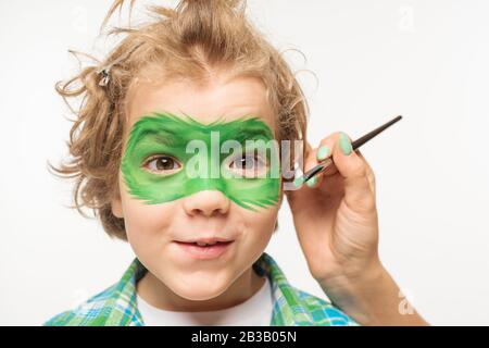 vista ritagliata della maschera gecko dell'artista sul volto di un ragazzo allegro e scrigno isolato su bianco Foto Stock