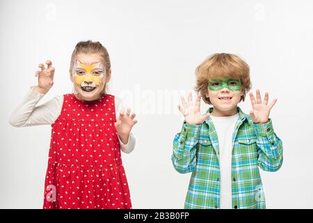 amici allegri con muso gatto e maschera gecko dipinti su volti che mostrano gesti spaventosi alla macchina fotografica isolato su bianco Foto Stock