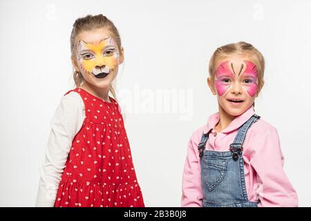 adorabili bambini con muso di gatto e dipinti a farfalla sui volti guardando la macchina fotografica isolata su bianco Foto Stock