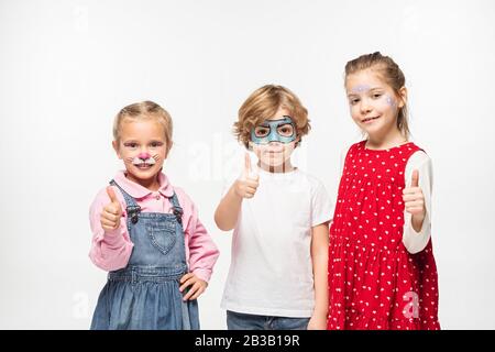 amici allegri con dipinti colorati che mostrano i pollici mentre si guarda la fotocamera isolata su bianco Foto Stock