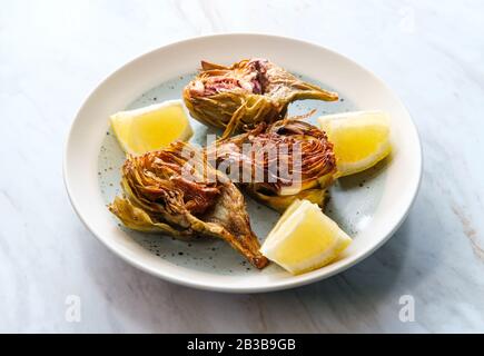 Carciofi fritti italiani tagliati a metà con spicchi di limone Foto Stock