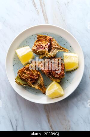 Carciofi fritti italiani tagliati a metà con spicchi di limone Foto Stock