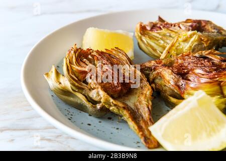 Carciofi fritti italiani tagliati a metà con spicchi di limone Foto Stock