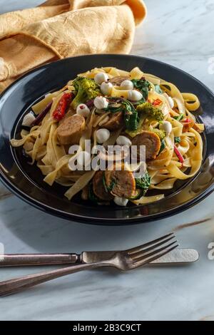 Salsiccia di pollo italiana fettuccina primavera in salsa all'aglio bianco con funghi broccoli baby kale pomodori secchi e minisine mozzare perline Foto Stock