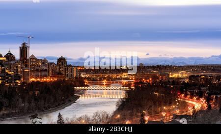 Calgary di notte, Alberta, Canada. Peace Bridge sul fiume Bow di notte, Calgary centro di notte autunno con il fiume in primo piano e le montagne in ba Foto Stock