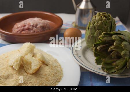 Primo piano degli ingredienti usati per cucinare carciofi farciti a casa. Abbiamo pangrattato, carne macinata, olio e uova su un tavolo di casa Foto Stock