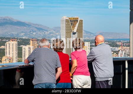 Due coppie anziane guardano l'alto complesso residenziale di appartamenti Intempo al sole con le sue montagne sullo sfondo, Benidorm, Spagna, Europa. Foto Stock