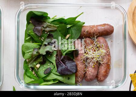 Vista dall'alto della scena di cottura a lotti centrata in un vaso pieno di salsicce con foglie di spinaci e germogli di soia. Foto Stock