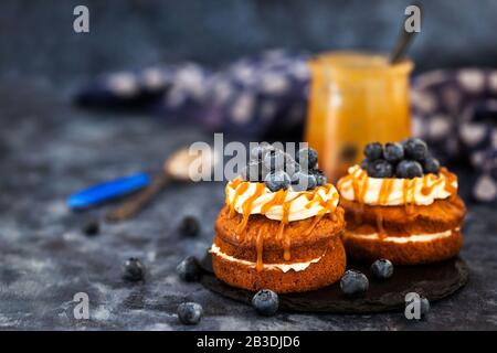 Torte individuali di carote fatte in casa con salsa al caramello, crema di formaggio glassa e mirtilli freschi Foto Stock