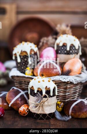 Dolci pasquali per le vacanze, focaccine di croce calda e colorate uova dipinte su sfondo rustico Foto Stock