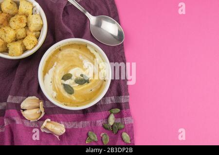 Zuppa di piselli con semi di zucca, accanto a verdure e crostini con aglio su un asciugamano viola Foto Stock