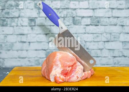 Un'ascia per la carne si trova in un grande pezzo di maiale succoso Foto Stock