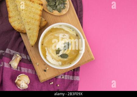 Zuppa di piselli con semi di zucca, accanto a verdure e crostini con aglio su un asciugamano viola Foto Stock