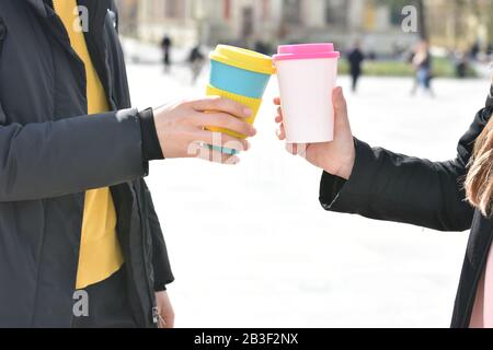 Due mani da donna che tengono eleganti tazze riutilizzabili per caffè ecologico all'aperto. . Foto Stock