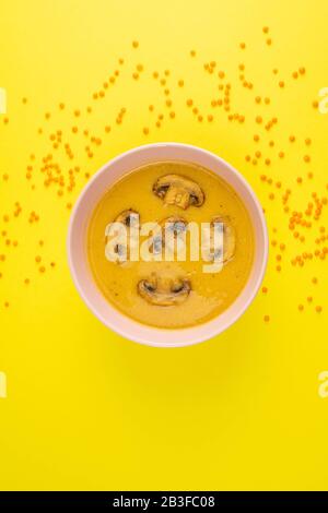 Zuppa di piselli con funghi in una piastra rosa si erge su uno sfondo giallo, intorno alla dispersione di semi di lenticchie Foto Stock