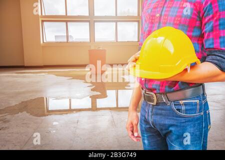 Ingegnere che tiene il casco di sicurezza giallo plastica e acqua perdita goccia sfondo interno ufficio Foto Stock