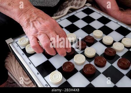 La mano di una vecchia nonna muove gli ispettori attraverso il campo di gioco. Dama Marrone E Bianca. Foto Stock