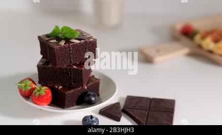 Vista ravvicinata della pila di brownie al cioccolato su piatto bianco con foglie di menta sulla parte superiore, fragole e mirtilli decorati Foto Stock