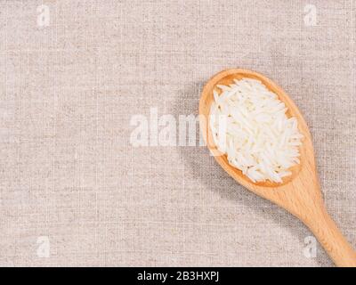 Riso indiano a grani lunghi Basmati in legno cucchiaio diagonalmente su sfondo di tessuto beige Foto Stock