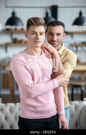 Uomo dai capelli scuri in camicia arancione che abbraccia il suo partner e si sente bene Foto Stock